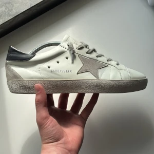  Golden Goose skor - Tjena! Säljer ett par vita sneakers från Golden Goose. Perfekta skor nu inför sommaren. Skorna har varit använda under typ en vecka. Skick 8/10. Inga defekter, som sagt knappt använda. Storlek 43. Hör av er vid minsta lilla fundering 🙌