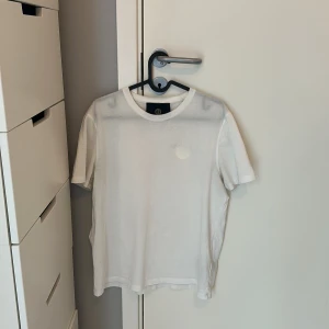 Vit t-shirt från Limitato S - Säljer en stilren vit t-shirt från Limitato med rund hals och diskret broderad logga på bröstet. T-shirten har en klassisk passform och är tillverkad i mjuk bomull. Perfekt basplagg till garderoben. Köpt på nk för 1399kr, box tags med mera finns