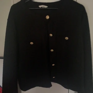 Svart kofta med guldknappar - Säljer en svart kofta med långa ärmar och guldknappar framtill. Koftan har rund halsringning och två fickor med knappar på bröstet. Den är i stl xxl men skulle säga att den är lite mindre i passformen. Perfekt tröja till en tråkig outfit man vill liva upp lite! Va inte rädd att lägga pris förslag!