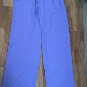 Ljuslila vida byxor med dragsko - Säljer ett par ljuslila byxor med bred passform och dragsko i midjan. Byxorna är tillverkade i ett tunt, mjukt tyg som känns skönt mot huden nästan som linen tyg. 