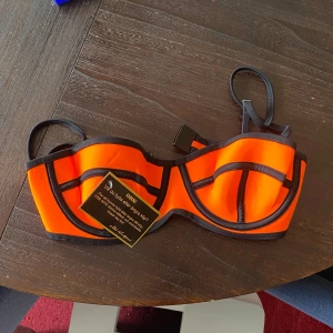 Orange bikiniöverdel med svarta kanter - Sån bikini som ser ut å va från 2010. Säljer för den är för liten i kupan för mig. Rekommenderar för ngn med A-B kupa. Lapp kvar. Var tvungen att så om ena spännet då den var sydd fast åt fel håll. Endast testad 