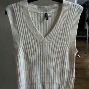 Vit ribbad stickad väst  - Säljer en vit stickad väst från H&M med bred ribbad struktur och djup v-ringning. Perfekt att styla över en skjorta eller t-shirt för en trendig lager-på-lager-look.