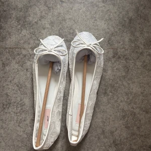 Vita spetsballerinaskor med rosett - Säljer ett par vita ballerinaskor med spetsdetaljer och söt rosett framtill. Skorna har platt sula och rund tå, perfekta för en elegant och feminin look. Passar till många olika tillfällen. Storlek 38 helt oandvända 