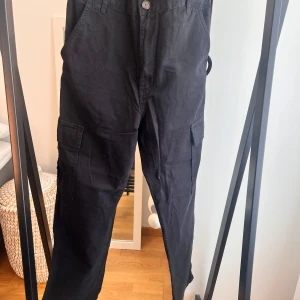 Stradivarius svarta cargo byxor, storlek 38 - Svarta byxor med fickor på sidorna och bakfickor. Byxorna har en knappstängning fram. Endast provad.