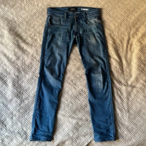 Blå Replay Anbass jeans slim fit - Säljer ett par blå Replay Anbass jeans med slim fit. Klassisk femficksmodell med dragkedja och knapp i midjan. Snygga slitningar framtill och bakfickor med diskret broderi. Perfekta för dig som gillar en smalare passform. Storlek: 31/32