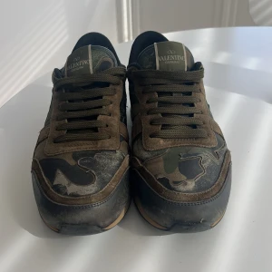 Valentino Rockrunner  - Säljer ett par Valentino Rockrunner sneakers med camouflage-mönster i grönt, brunt och svart. Skorna har gröna snören, rund tå och detaljer i ljusblått och grönt på hälen. Klassisk gummisula och ikoniska nitar baktill. definitivt tecken på användning, kommer med extra snören och dustbag! 