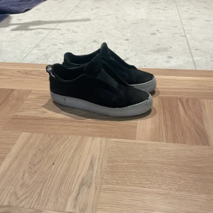 Svarta arigatos från arigato  - Svarta sneakers i slip-on-modell med vit, platt sula. Skorna har en minimalistisk design utan snörning och är tillverkade i syntetmaterial. Perfekta för en avslappnad och stilren look. Dom är sönder lite i bak men de är inget man tänker på annars är dom bra skick dom är från arigato och har box o dust bag🤩