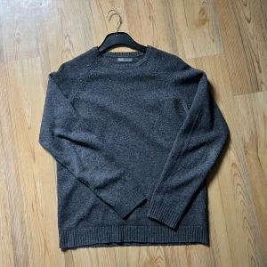 Mörkgrå stickad tröja från ASOS - Mysig mörkgrå stickad tröja från ASOS med rund halsringning och ribbade muddar vid ärmslut och nederkant. Perfekt för kyligare dagar och enkel att matcha med olika outfits.