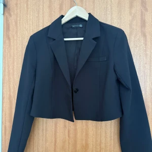 Svart croppad kavaj - Snygg svart croppad kavaj från Dazy med klassisk krage och en knapp framtill. 