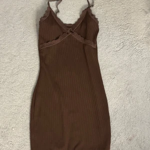 Brun klänning med spetsdetaljer från H&M Divided - Säljer en brun klänning från H&M Divided med smala axelband och spetsdetaljer vid bysten. Klänningen har en tight passform och är kort i modellen, perfekt för en trendig look. 