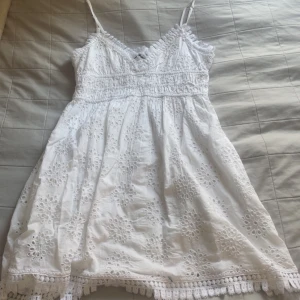 Vit sommarklänning från Gina Tricot - Superfin vit klänning från Gina Tricot med broderade blommor och spetsdetaljer. Klänningen är ärmlös med smala axelband och har en v-ringad halsringning. Perfekt för midsommar eller avslutnings klänning☀️🩷 hade den förra året på skolavslutningen🩷