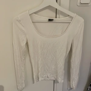 Vit långärmad topp med rund hals - En enkel och stilren vit långärmad topp med rundad, djup urringning. Tunn och mjuk i materialet. Armarna har slits längst ut Storlek S
