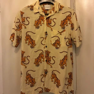 Beige skjorta med tryck - Säljer en beige skjorta från carlings med  tigertryck i orange och svart. Skjortan har klassisk krage, knäppning framtill och en bröstficka.  Strl S