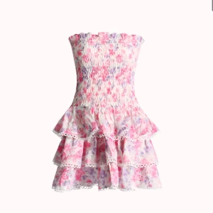  axelbandslös volangklänning - Supersöt axelbandslös klänning med blommigt mönster i rosa, lila och vitt. Klänningen har smock upptill och flera volanglager med spetsdetaljer. Perfekt för sommarens alla tillfällen!