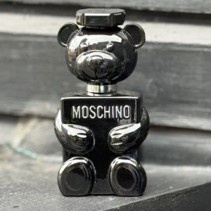 Moschino Toy Boy Eau de Parfum 100ml - Moschino Toy Boy är en herrparfym i en unik svart björnformad flaska. Flaskan rymmer 100 ml och har en glänsande finish med tydlig Moschino-logga framtill. Parfymen är en Eau de Parfum och passar dig som gillar lekfull design och exklusiva dofter. Helt ny och säljer den för jag fick den i present och jag tyckte inte om den.