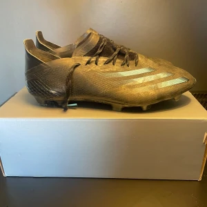 Adidas X Speedflow fotbollsskor i svart och turkos - Säljer ett par Adidas X Speedflow fotbollsskor i svart med turkosa detaljer och snörning. Skorna har en låg profil, platt sula med dobbar och är tillverkade i syntetmaterial. Perfekta för dig som vill ha lätta och snabba skor på planen.