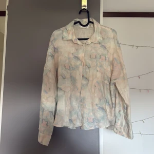 Pastellmönstrad linneskjorta från Lis Bonne Atelier - Säljer en tunn och luftig skjorta i linne från Lis Bonne Atelier. Skjortan har ett abstrakt pastellmönster i ljusa toner av blått, rosa och beige. Klassisk krage, knäppning framtill och långa ärmar med manschett. Perfekt för en avslappnad och stilren look. Liten fläck på insidan av vänstra ärmen, går förmodligen bort i tvätten (upptäckte när jag fotade tröjan, så lite har den synts)