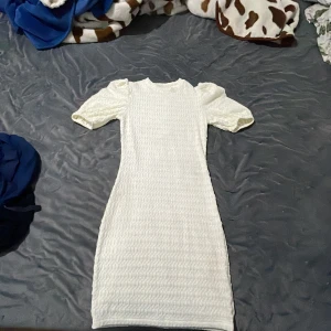 Vit ribbad kortklänning med puffärm - Säljer en söt vit kortklänning med puffärmar och ribbad struktur. Klänningen har en tight passform och är perfekt för sommarens alla tillfällen. Materialet är mjukt och stretchigt för extra komfort.