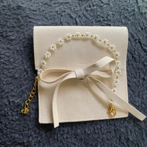 Blommigt armband med pärlor och gulddetaljer - Sött armband med små vita blommor av pärlor och guldfärgad kedja. Blommorna har gul mitt och armbandet stängs med en guldfärgad karbinhake. Perfekt accessoar inför sommaren. Sametspåse medföljer.