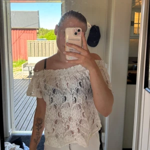 Vit spetsblus med offshoulder - Säljer en romantisk vit blus i spets med offshoulder-design. Blusen har korta ärmar och ett luftigt, volangigt fall. Perfekt för varma dagar och ger en bohemisk känsla.