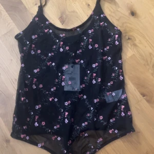 Svart blommig body från bikbok  - svart body från BikBok med tunna axelband och blommigt mönster i rosa och lila. den är genomskinlig och stretchig
