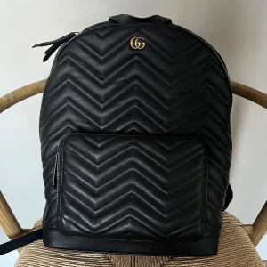 Svart ryggsäck/väska - Stor svart ryggsäck. Knappt använd men lite tilltryckt pga legat i en flyttlåda. Går säkert att bort vid användning. Har någon fläck inuti väskan, liten skada på undersidan. Finns ett datorfack.  Ej äkta. Höjd: 40 cm Bredd: 32 cm Djup: 13 cm