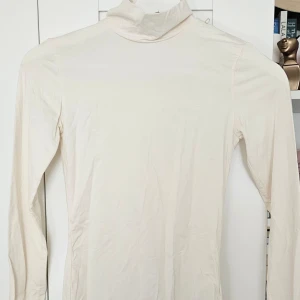 Vit polotröja i bomull - Säljer en enkel och stilren vit polotröja med lång ärm. Tröjan är i mjuk bomull och har en tight passform som sitter snyggt på kroppen. Perfekt att styla med jeans eller kjol för en clean look.