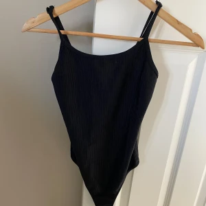 Svart ribbad body från Bik Bok - Säljer en svart ribbad body från Bik Bok i storlek XS. Toppen har smala axelband och är perfekt för sommaren. Enkel och stilren design som passar till mycket.
