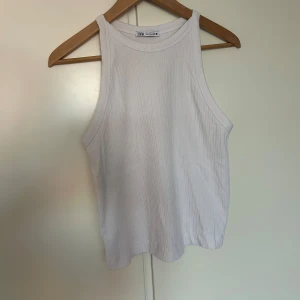 Vit ribbad linnetopp från Zara - Säljer en vit ribbad linnetopp från Zara. Toppen har en klassisk ärmlös design med rund halsringning och är tillverkad i ett mjukt, stretchigt material. Perfekt för varma dagar eller som lager under en skjorta.