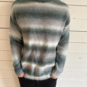 Gråmelerad stickad tröja - Säljer en stickad tröja i gråmelerade toner med inslag av grönt och vitt. Tröjan har lång ärm och rund halsringning. Perfekt för dig som gillar en avslappnad och stilren look. Storlek S men är ganska stor i storleken. Helt ny med lapp!