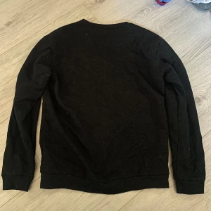 Svart basic tröja - En enkel svart tröja med rund halsringning och långa ärmar. Perfekt för lager-på-lager eller som den är. Mjuk och bekväm med ribbade muddar vid ärmslut och nederkant.