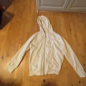 Vit hoodie från H&M - Säljer en enkel och stilren vit hoodie från H&M i storlek L men passar bra på mig som är S-M. Tröjan har dragkedja framtill, huva med dragsko och två fickor. Perfekt för en avslappnad look.