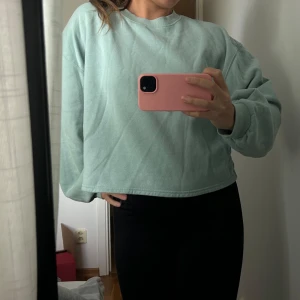 Mintgrön croppad sweatshirt - Säljer en mintgrön croppad sweatshirt med rund hals och långa ärmar. Tröjan har en avslappnad passform och är tillverkad i mjukt bomullsmaterial. Perfekt för en chill och stilren look.