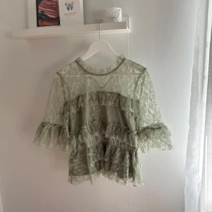 Grön spetsblus med volanger från Bubbleroom - Säljer en ljusgrön blus från Bubbleroom i spets med volangdetaljer i storlek 40. Den har ett litet hål i ena armen men de syns inte då de smälter in i spetsen💫 