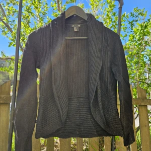 Svart ribbad cardigan  - Svart cardigan med ribbad struktur och lång ärm. Den har en öppen front utan knäppning och en mjuk, följsam passform. Perfekt för lager-på-lager och enkel att styla till olika outfits.