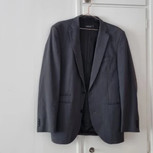 Grå kavaj från Ljung - Säljer en stilren grå kavaj från Ljung i storlek  XL LKavajen har klassisk passform med två knappar framtill, fickor med lock och innerficka. Perfekt för jobb eller business casual. Materialet känns mjukt och har en lätt struktur. Helt oanvänd