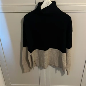 Svart och beige stickad polotröja från Vila - Säljer en snygg stickad polotröja i svart och beige. Tröjan har en hög krage och är tvåfärgad med svart upptill och beige nedtill samt på ärmarna. Perfekt för kyliga dagar och passar till det mesta.