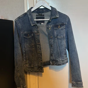 Mörkblå jeansjacka från Only - Säljer en klassisk mörkblå jeansjacka från Only. Jag skulle säga att den passar även Xs/S. Jackan har två bröstfickor med lock och knappar, samt knappstängning framtill. Modellen är croppad och har långa ärmar. Perfekt till vår och sommar!
