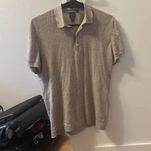 Beige t- skirt från H&M - Säljer en stilren beige pikétröja från H&M i bomull. Tröjan har korta ärmar, klassisk krage och knäppning med två knappar framtill. Perfekt för en avslappnad men snygg look.