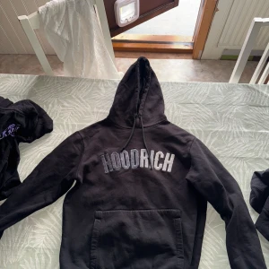 Svart hoodie från Hoodrich - Säljer en svart hoodie från Hoodrich i storlek M. Tröjan har en stor huva, magficka och HOODRICH-tryck i vitt på bröstet. Perfekt för en avslappnad och cool stil.