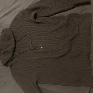 Svart stickad hoodie från Moncler - Säljer en svart stickad hoodie från Moncler med dragsko i huvan och diskret logga på ärmen. Tröjan har lång ärm och en klassisk passform som passar perfekt till kyliga dagar.