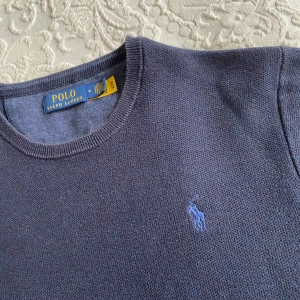 Mörkblå stickad tröja från Polo Ralph Lauren - Säljer en klassisk mörkblå stickad tröja från Polo Ralph Lauren med rund halsringning och broderad logga på bröstet. Perfekt för en stilren och avslappnad look. Tröjan har långa ärmar och ribbade muddar. Ny pris ligger på ca 1900