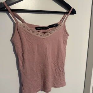 Rosa linnetopp med spets - Säljer en söt rosa linnetopp från The Blue Label Club. Toppen har smala axelband och en fin spetsdetalj längs v-ringningen framtill. Perfekt för varma dagar eller som lager under en kofta.