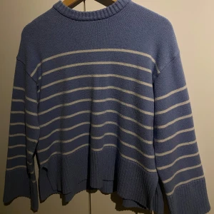 Blå och vit randig stickad tröja - Säljer en blå stickad tröja med vita horisontella ränder. Tröjan har lång ärm, rund halsringning och ribbade muddar vid ärmslut och nederkant. Perfekt för kyligare dagar och enkel att matcha med jeans eller kjol.