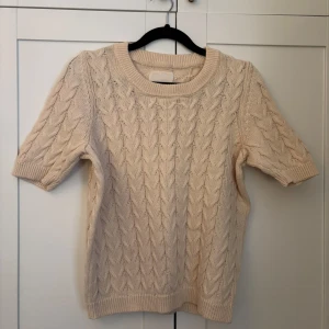 Beige stickad kortärmad tröja från Part Two - Säljer en beige stickad tröja från Part Two i storlek XS. Tröjan har korta ärmar och ett klassiskt kabelstickat mönster. Perfekt för lager-på-lager och passar till många olika stilar. Supermjuk och skön att bära!