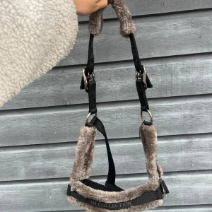 Grått och svart fluffig grimma häst - Säljer en mjuk och fodrad grimma från JH Collection i grått och svart. Perfekt för att ge extra komfort till hästen. Justerbara spännen i metall och fluffigt material på insidan. I storlek ponny