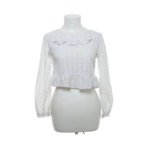 Vit spetsblus från Zara Woman - Säljer en söt vit blus från Zara Woman med spetsdetaljer och volang vid bröstet och nederkanten. Blusen har lång ärm och är tillverkad i ett broderat tyg som ger en romantisk känsla. Perfekt för dig som gillar feminina detaljer.