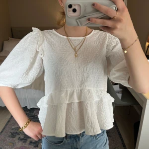Vit volangblus med puffärm - Superfin vit blus med puffärmar och volangdetaljer. Blusen har en strukturerad yta och rund halsringning. Perfekt att styla med jeans eller kjol!🤍🍓 
