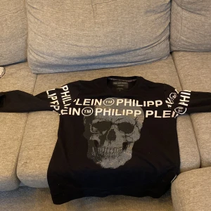 Svart tröja med döskalle från Philipp Plein - Säljer en svart långärmad tröja från Philipp Plein med glittrig döskalle framtill och logga i vitt på ärmar och bröst. Tröjan har rund halsringning och är i mjukt material. Perfekt för dig som gillar statement-plagg!