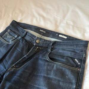 Mörkblå Replay jeansbyxor - Säljer ett par mörkblå jeans från Replay med klassisk femficksdesign och snygga kontrastsömmar. Byxorna har normal passform och raka ben, med Replay-logga på fickan och läderpatch bak i midjan.